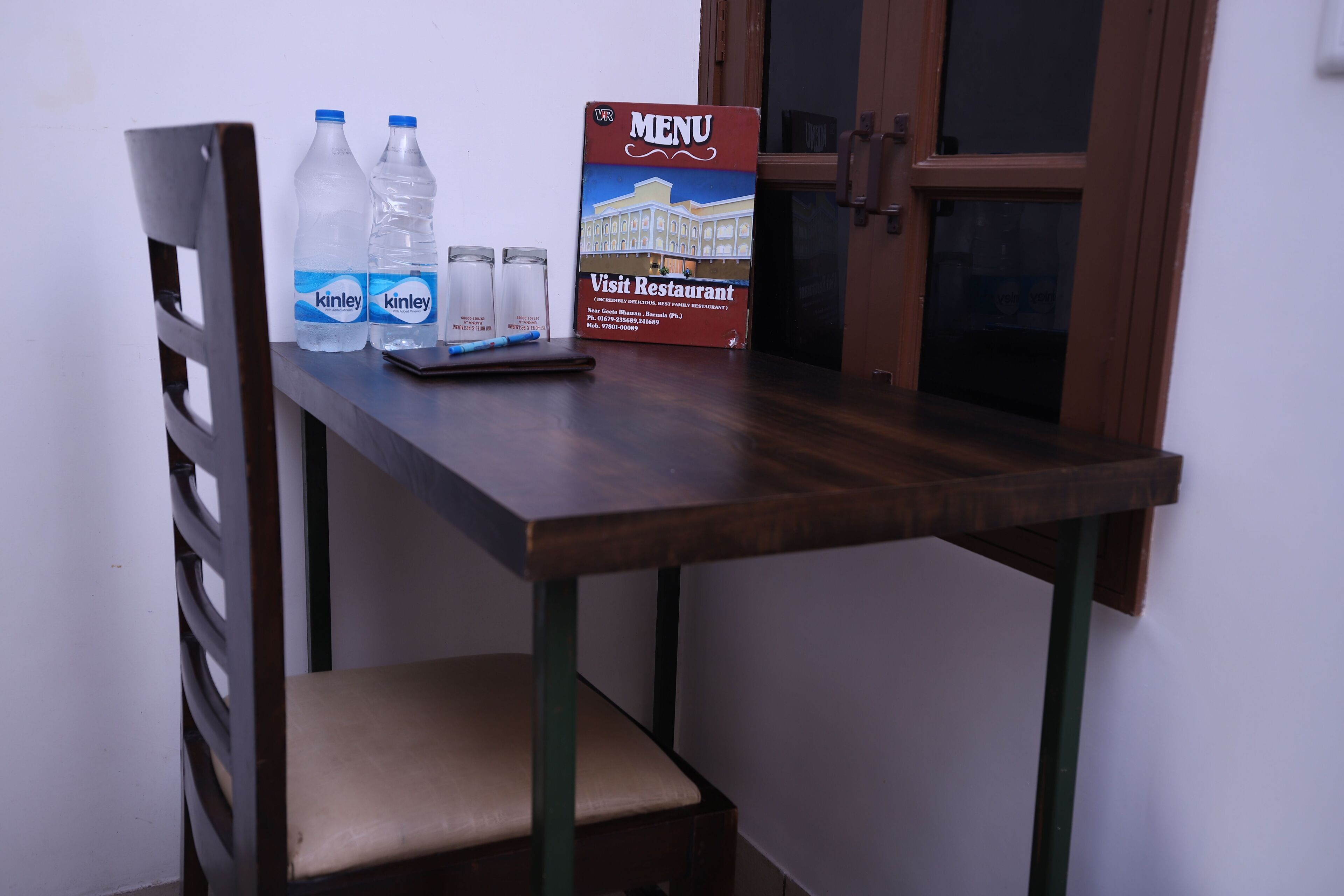 A wooden table with a menu sign, two Kinley water bottles, and a smartphone.
