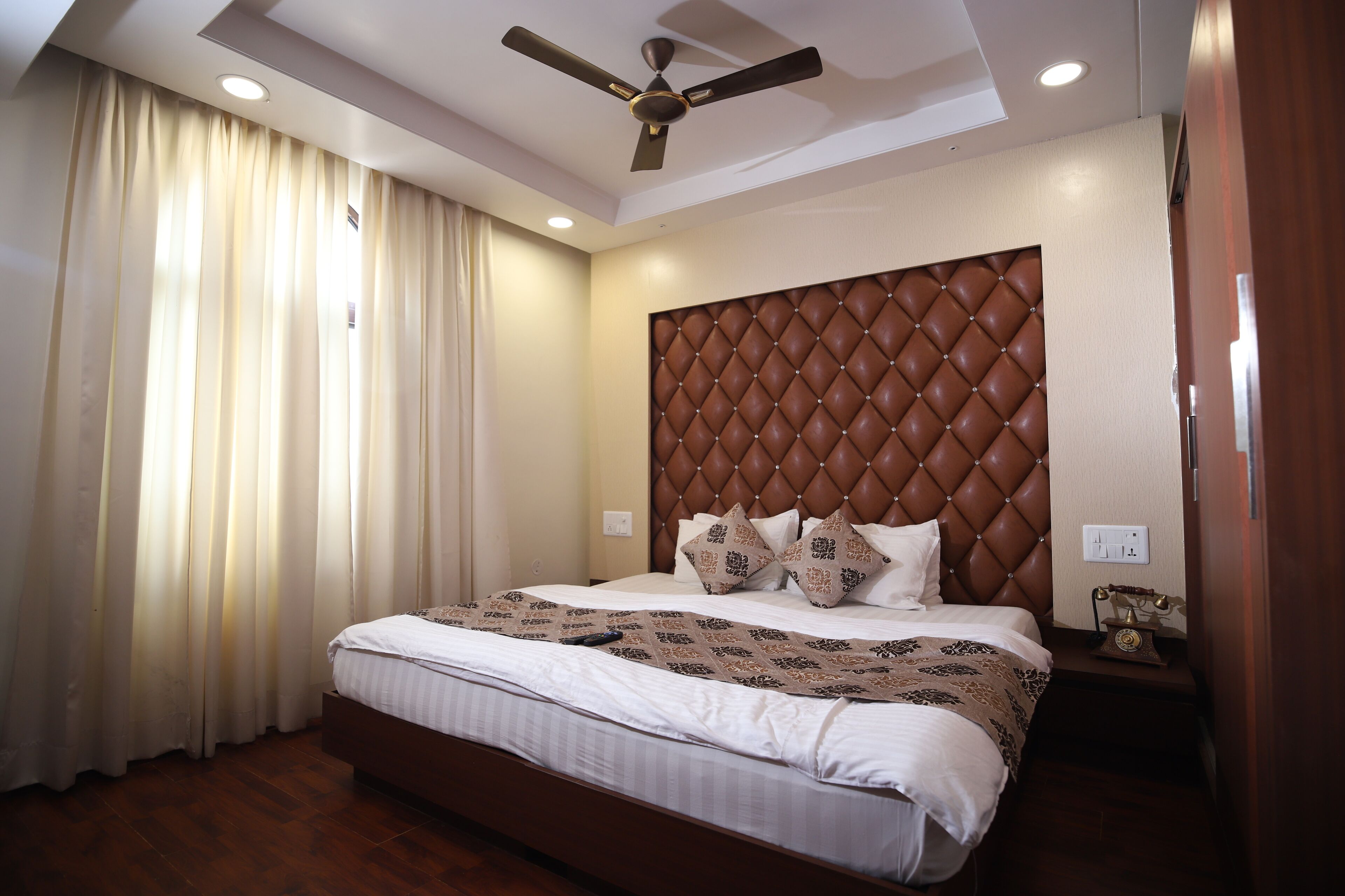 A hotel room with a large bed, a ceiling fan, a nightstand with a telephone, and a window with curtains.