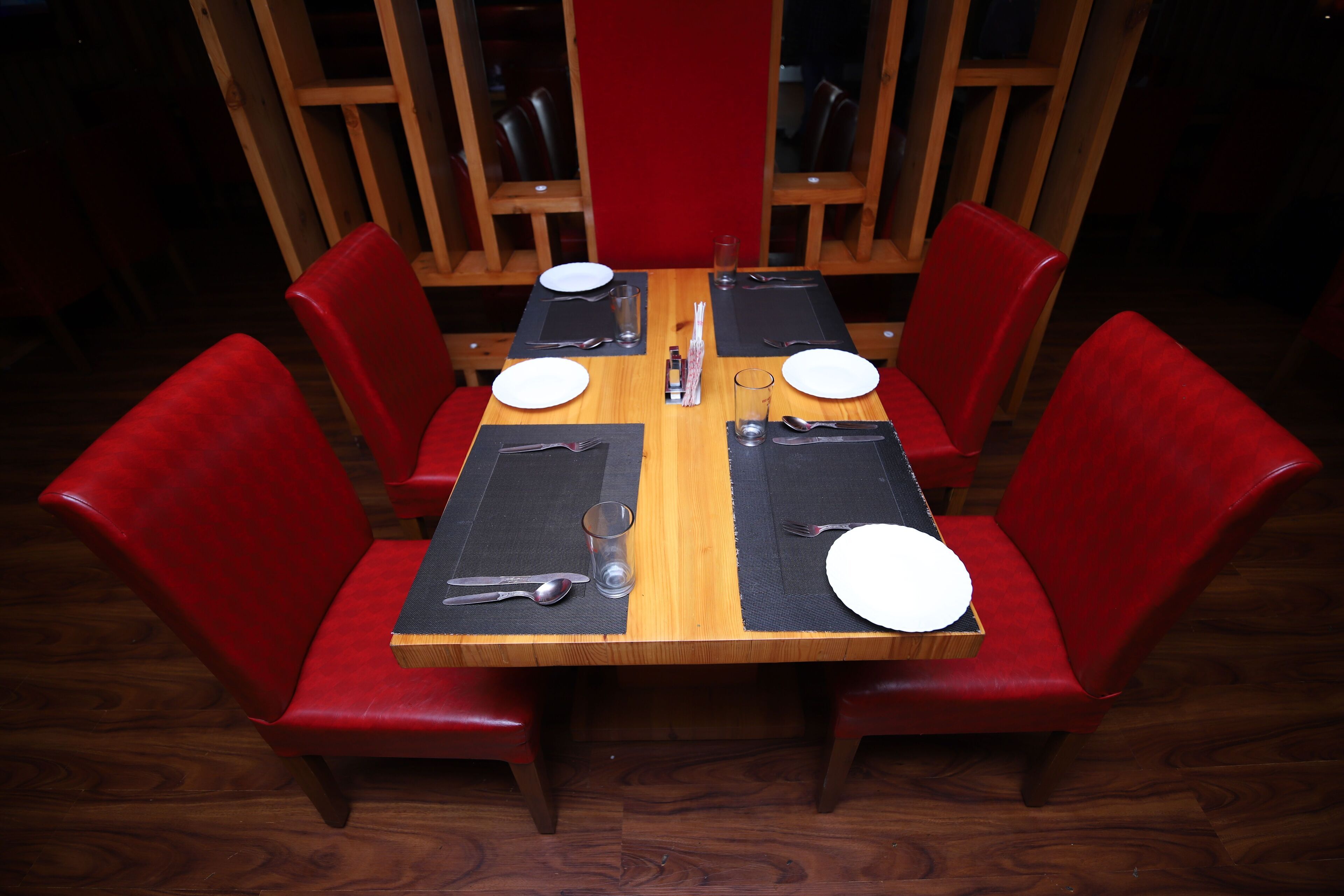 A dining table with four red chairs, black placemats, and silverware.