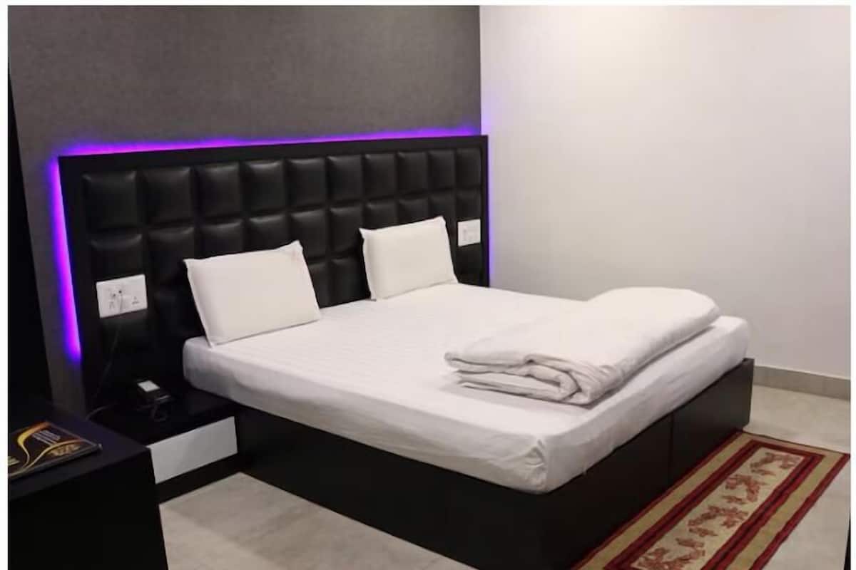 Une chambre à coucher moderne avec une tête de lit noire, du linge de lit blanc et un tapis à motifs rouges et beiges.