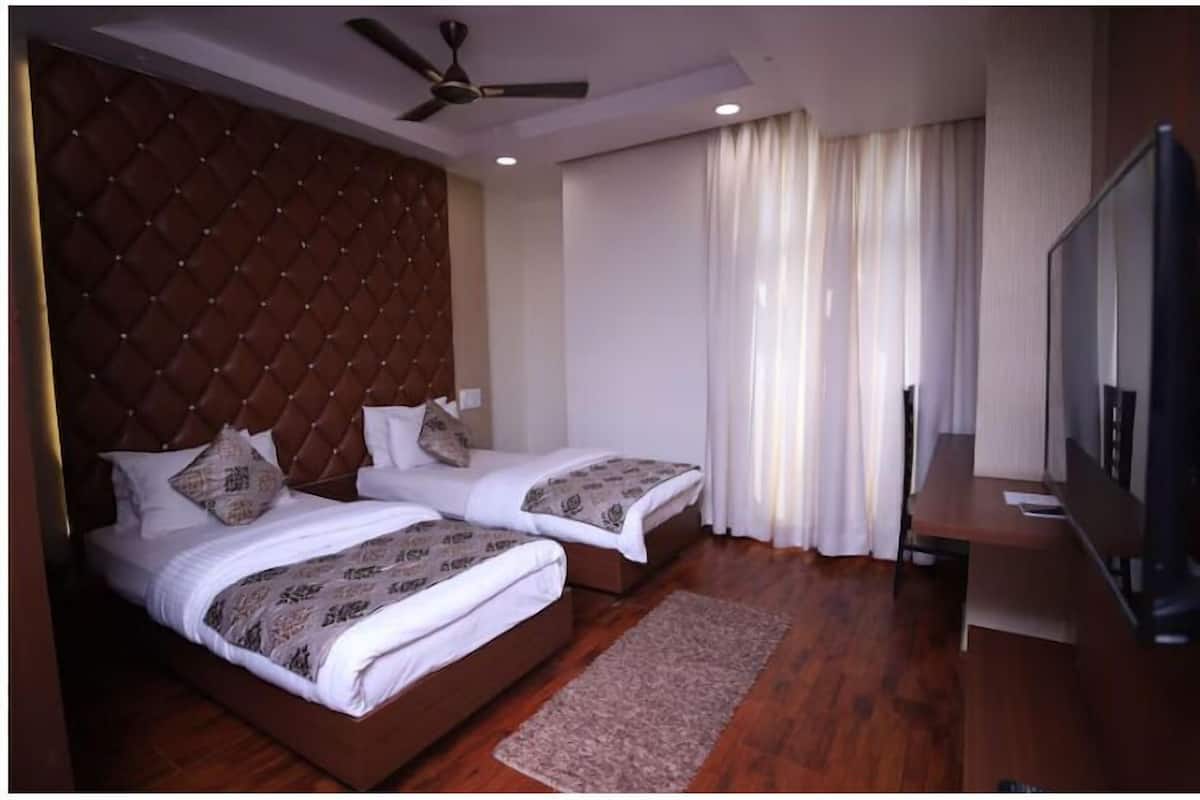 Une chambre d’hôtel avec deux lits, un ventilateur de plafond, une télévision et une grande fenêtre avec des rideaux.