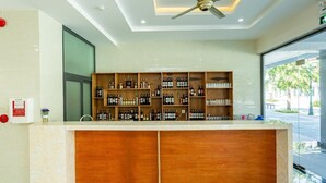A hotel reception area with a marble counter, wooden shelving with liquor bottles, a ceiling fan, and a large window offering a view of the street. - Mai Hùng Hotel (Phu Quoc)