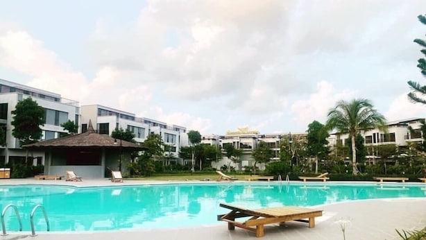 A swimming pool with lounge chairs, surrounded by modern buildings and palm trees. - Mai Hùng Hotel (Phu Quoc)