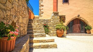 A stone staircase leading to a building with a wooden door and a window with a metal railing. - Four bedroom Mouri villas complex of 18th century (CPM2+9RH Mouri, Greece)