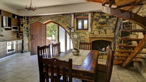 A rustic kitchen with stone walls, a wooden dining table, and a spiral staircase. - Four bedroom Mouri villas complex of 18th century (CPM2+9RH Mouri, Greece)