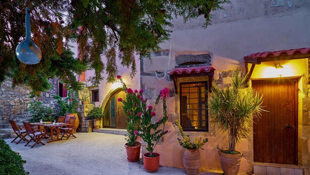 An outdoor patio with a table and chairs, potted plants, and a wooden door. - Four bedroom Mouri villas complex of 18th century (CPM2+9RH Mouri, Greece)