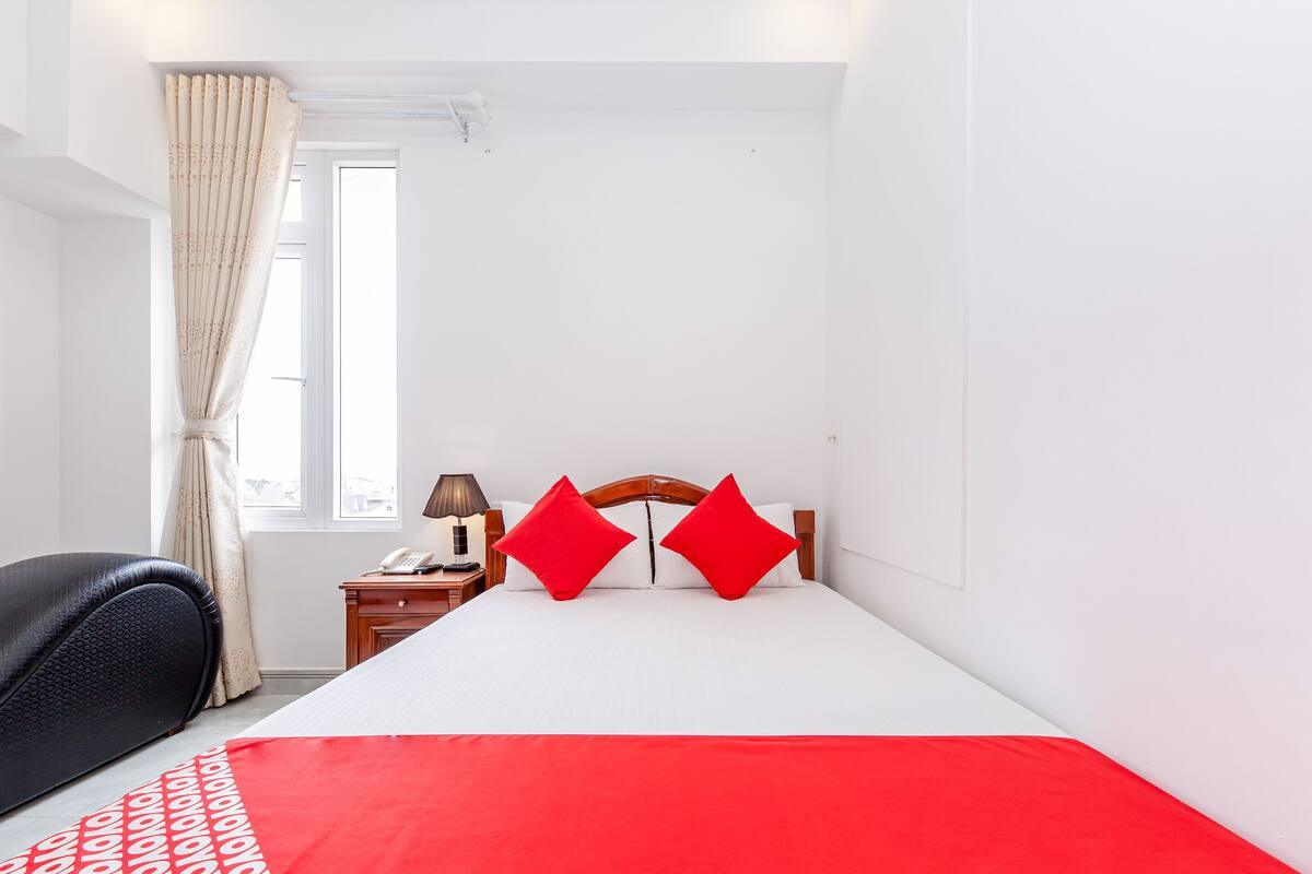 A hotel room with a bed, a nightstand, a lamp, a chair, and a window with curtains.