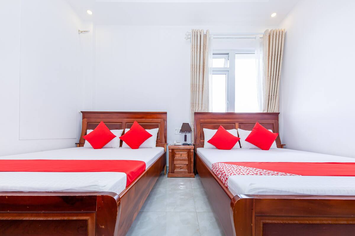 A hotel room with two beds, each with red and white bedding, a nightstand with a lamp, and a window with curtains.
