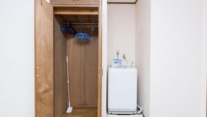 A laundry room with a washing machine, a mop, and a blue laundry basket. - Centrally Located Deluxe Furnished.3 (Tokyo)