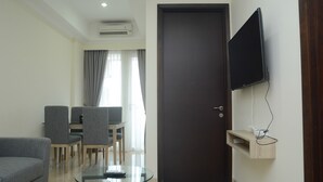 A modern living room with a glass coffee table, grey sofa, and a flat-screen TV mounted on the wall. - Wonderful 2BR at Menteng Park Apartment (Jakarta)