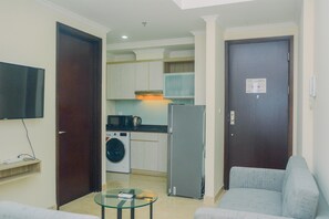 A compact living space with a kitchenette, a washing machine, a refrigerator, a flat-screen TV, and a glass coffee table.