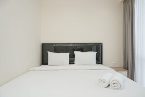 A neatly made bed with white linens and two pillows, a wooden nightstand with a lamp, and a window with curtains.