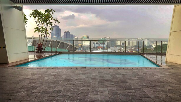 Une piscine sur le toit offrant une vue sur la ville, entourée d’un sol carrelé et d’une rambarde en verre.