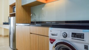 Une cuisine de taille réduite, dotée de meubles en bois, d’un réfrigérateur en acier inoxydable et d’un lave-linge.