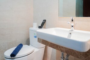 A bathroom with a white toilet, sink, and mirror, featuring a towel neatly rolled on the toilet seat.