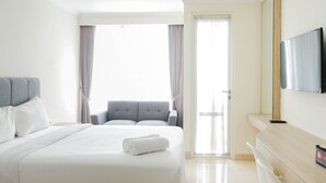 Ein Hotelzimmer mit einem großen Bett, einer Sitzecke mit grauem Polsofa, einem flachbildfernseher an der Wand und einer Tür, die auf einen Balkon führt.