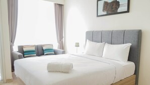 A neatly made bed with white linens and a folded towel, a grey upholstered sofa with striped cushions, and a framed picture on the wall. - Newly Furnished Studio Apartment at Menteng Park (Jakarta)