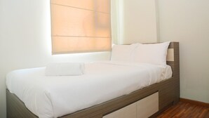 A neatly made bed with white linens and pillows, a wooden headboard, and a window with blinds. - Best Choice 2BR Apartment at Menteng Square (Jakarta)