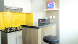A compact kitchen with a gas stove, a microwave, and a travelio box on the counter. - Best Choice 2BR Apartment at Menteng Square (Jakarta)