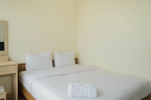 A neatly made bed with white linens and two pillows, a wooden nightstand with a mirror, and a folded white towel on the bed.