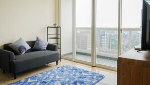 Un soggiorno moderno con un divano grigio, un tappeto azzurro decorato, un mobile TV in legno e un'ampia finestra con vista sulla città.