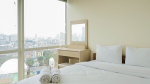 Una camera d'albergo con un'ampia finestra, un letto con lenzuola bianche, un comodino in legno, uno specchio e vista sulla città.