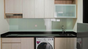 Una cucina compatta con mobili in legno, lavatrice integrata e piano di lavoro nero.