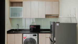 A compact kitchen with a washing machine, a microwave, and a refrigerator. - Wonderful 2BR Menteng Park Apartment with Private Lift (Jakarta)