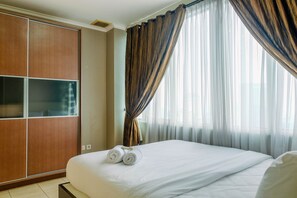 Habitación de hotel con cama, armario y ventana con cortinas.