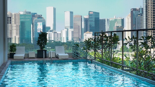 A rooftop infinity pool with a city skyline view, lounge chairs, and potted plants.