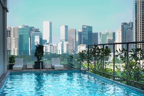 Una piscina infinita en la azotea con vistas al horizonte de la ciudad, sillas de descanso y plantas en macetas.