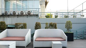 A rooftop terrace with two white wicker sofas and a matching ottoman, a staircase, and potted plants.