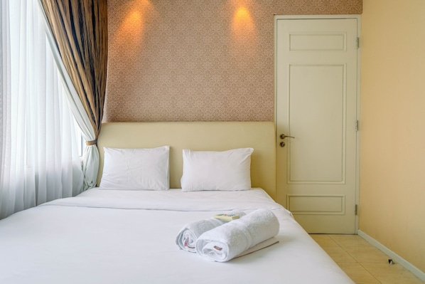 Habitación de hotel con cama, dos almohadas, una puerta y una toalla sobre la cama.