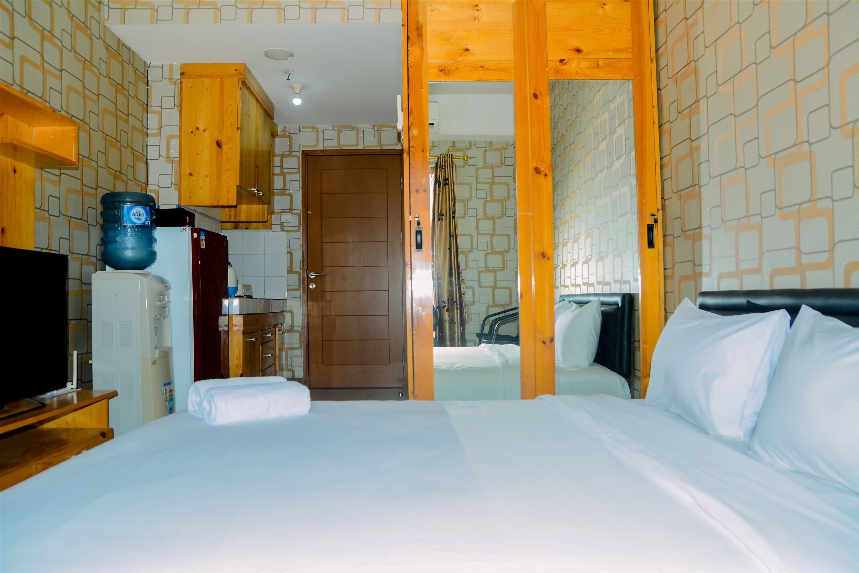 A hotel room with a bed, a TV, a water dispenser, and wooden cabinets.
