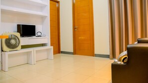 A room with a white entertainment unit, a television, a fan, and two wooden doors. - Gading Greenhill 2BR Apartment near Singapore International School (Jakarta)