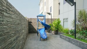 A courtyard with a blue slide, a brick wall, and a building with multiple windows. - Gading Greenhill 2BR Apartment near Singapore International School (Jakarta)