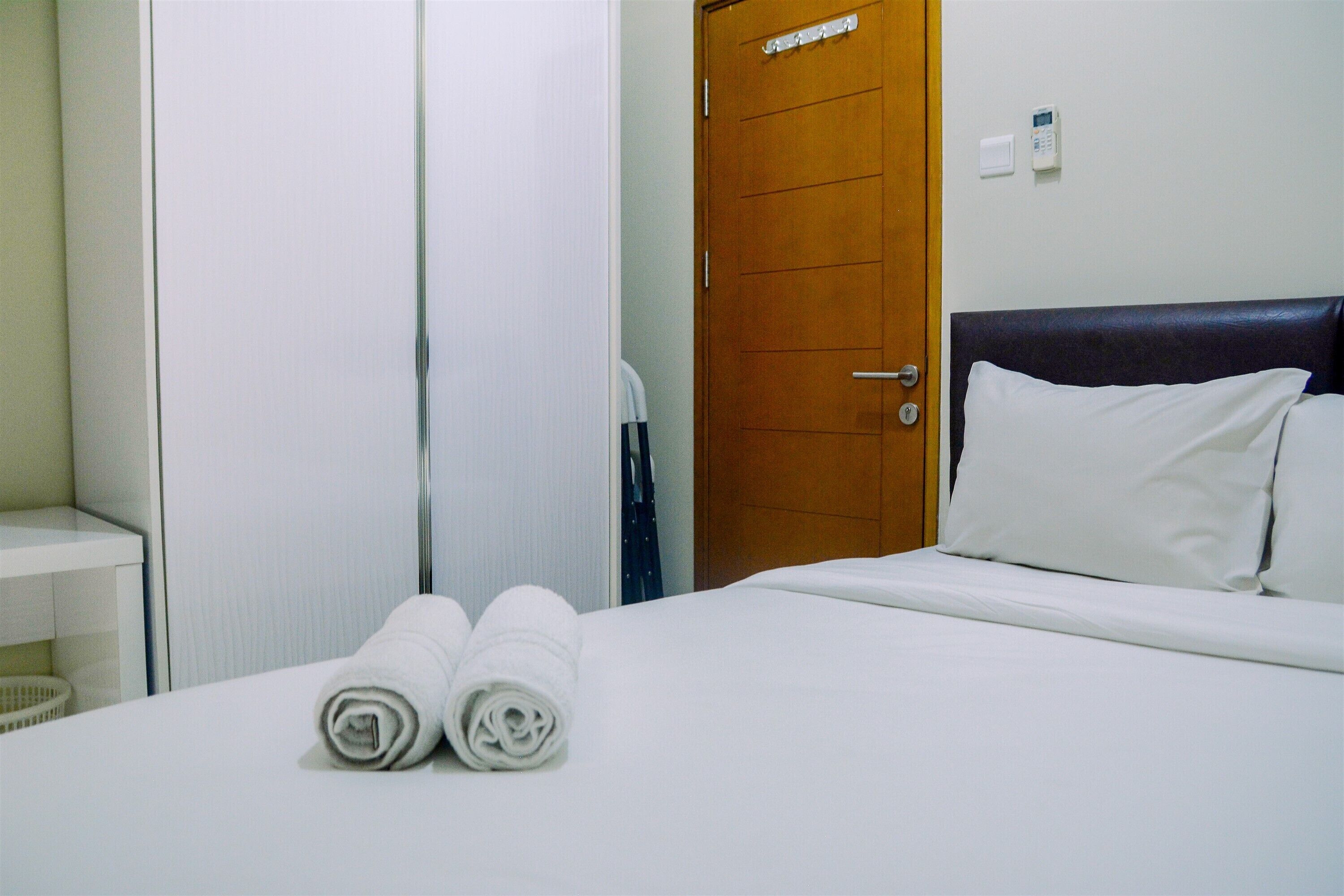 Habitación de hotel con una cama bien tendida, una puerta de madera y una pared blanca con un termostato.