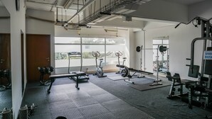A gym with various exercise equipment, large windows, and a ceiling with exposed pipes and ducts. - Gading Greenhill 2BR Apartment near Singapore International School (Jakarta)