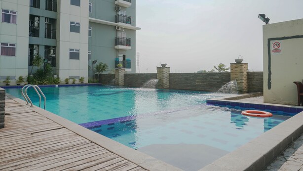 A swimming pool with a wooden deck, a no-smoking sign, and a building with balconies in the background. - Gading Greenhill 2BR Apartment near Singapore International School (Jakarta)