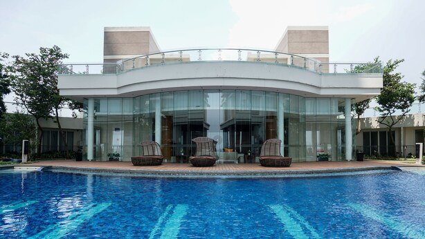 A modern building with a glass facade, a swimming pool in front, and outdoor seating.