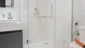 A modern bathroom with a glass-enclosed shower, a white sink, and a toilet.