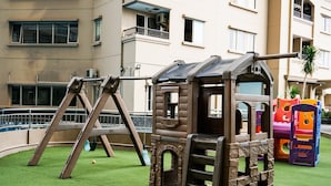 A children's play area with a wooden playhouse, swings, and colorful play structures. - 2BR for 3 Pax Mediterania Marina Ancol Apartment (Jakarta)