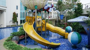 A children's play area with slides and climbing structures, surrounded by a pool and greenery. - Comfortable and Homey 1BR Apartment at Ancol Mansion (Jakarta)