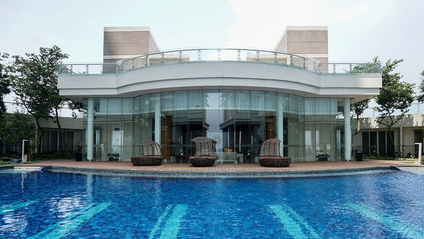 A modern building with a curved glass facade, a swimming pool in front, and outdoor seating. - Comfortable and Homey 1BR Apartment at Ancol Mansion (Jakarta)