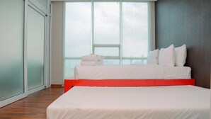 A modern hotel room with a large bed, a red headboard, and a view through a large window. - Comfortable and Homey 1BR Apartment at Ancol Mansion (Jakarta)
