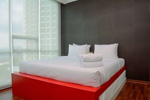 Une chambre d’hôtel moderne avec un grand lit, du linge de lit blanc et un lit surélevé avec une structure rouge.