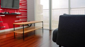 A modern room with a red wall, a flat-screen TV mounted above a wooden table, and a grey sofa. - Comfortable and Homey 1BR Apartment at Ancol Mansion (Jakarta)