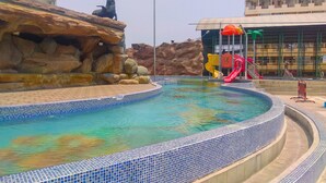 A swimming pool with a tiled edge, a rock formation, and a playground with slides. - Comfy 1BR Teluk Intan Apartment (Jakarta)