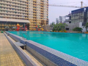 A swimming pool with a tiled edge, a children's play area with slides, and a high-rise building in the background. - Comfy 1BR Teluk Intan Apartment (Jakarta)
