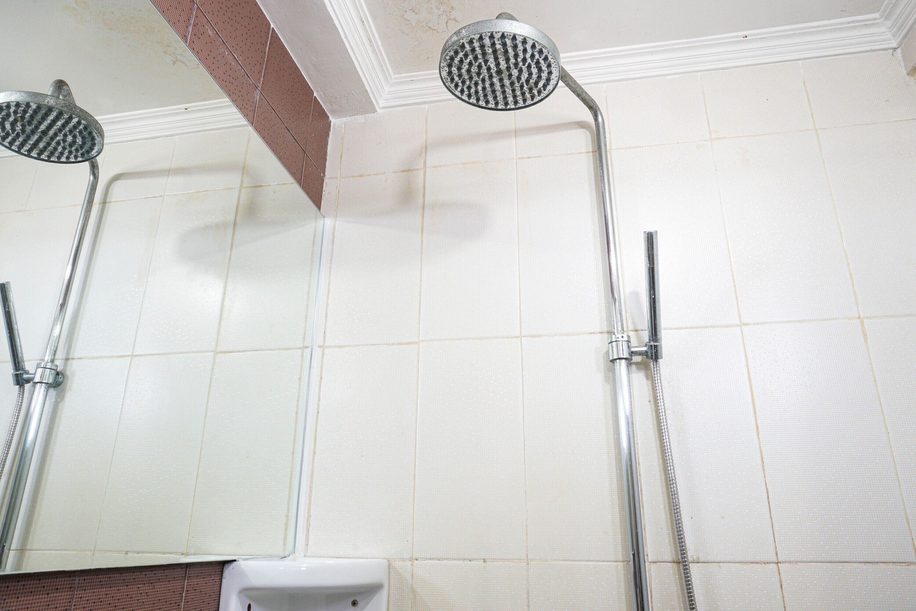 A bathroom with two showerheads mounted on the wall, a white toilet, and a tiled floor.